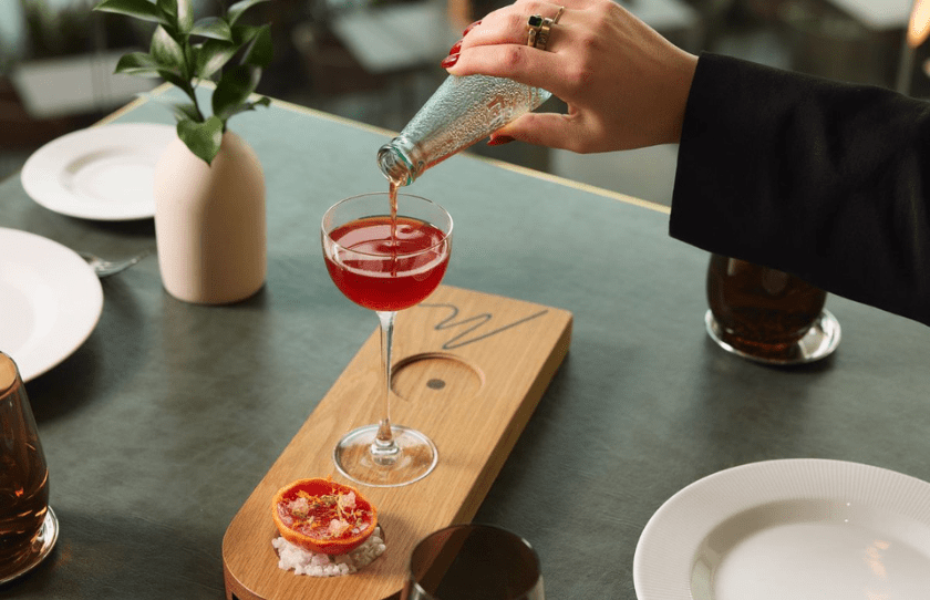 woman pouring Negroni Cocktail tableside into ice-cold glasses