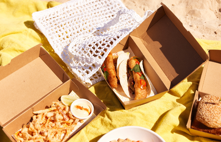 Selection of North Bondi Fish takeaway dishes including fish tacos and chips on a yellow beach towel.