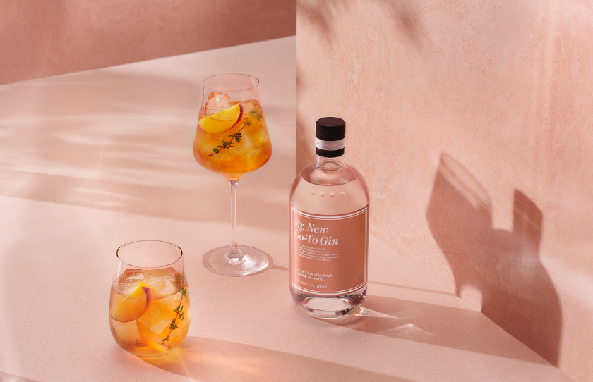 New limited edition Go-To Gin bottle against peach pink background paired alongside two gin spritz glasses with peach.