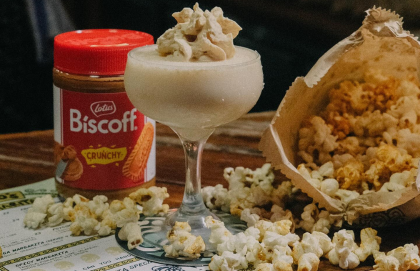 Frozen Biscoff and coconut margarita surrounded by popcorn falling out of a paper bag with a jar of Biscoff in the background at Tio's in Surry Hills