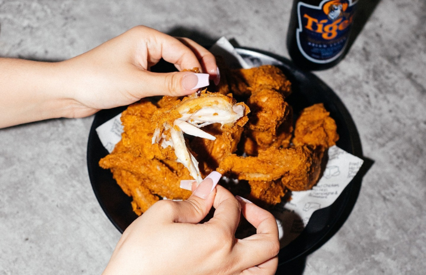 Chicken wings being torn apart by a girl with long fingernails from Butter Sydney and a Tiger beer in the background