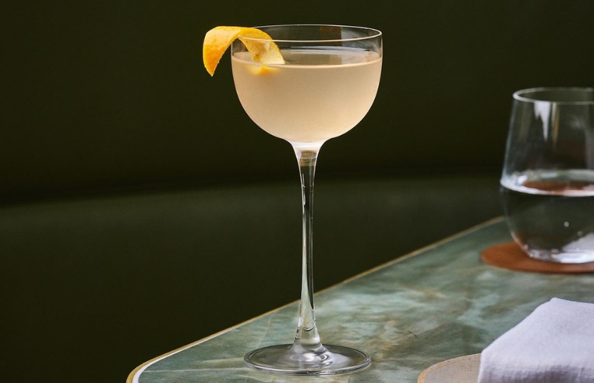 Gildas cocktail with orange twist garnish in a martini glass on a marble top counter