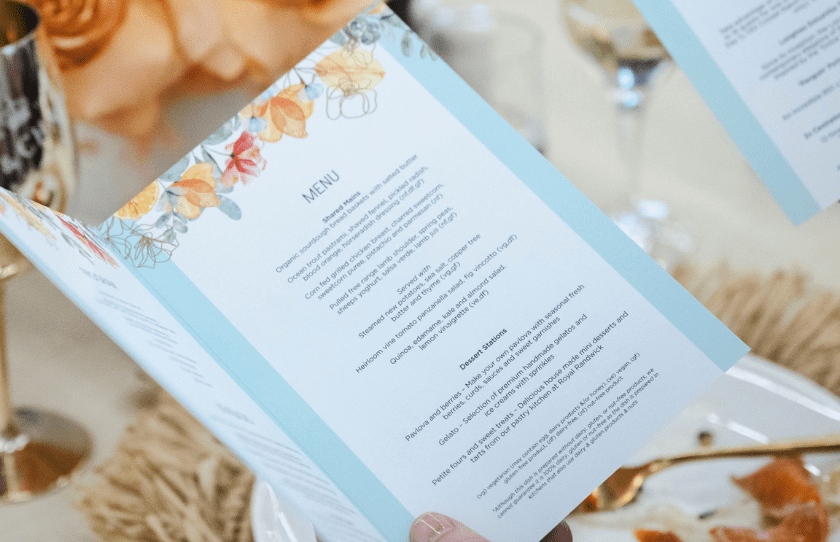 woman holding a menu with flowers in the background. menu is a shared style and includes desert station for Sydney Everest carnival long lunch at the Australian Turf Club. 