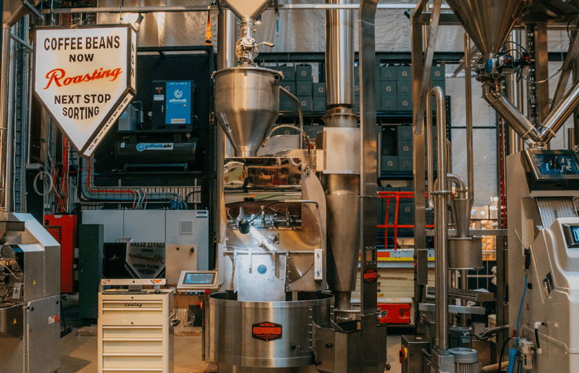 coffee roaster in factory. sign reads coffee beans now roasting