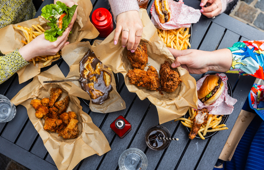 Image of food from Mary's - fried chicken, fries, gravy, condiments on a picnic table with soft drinks and hands. Victoria Cross North Sydney venue.