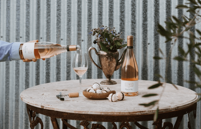 Lowe rose being poured into a wine glass with a bottle on the table too, in front of a striped wall. October Drinks Guide 2024